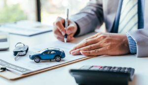 Driver reviews a car loan statement and auto insurance documents beside a parked vehicle.