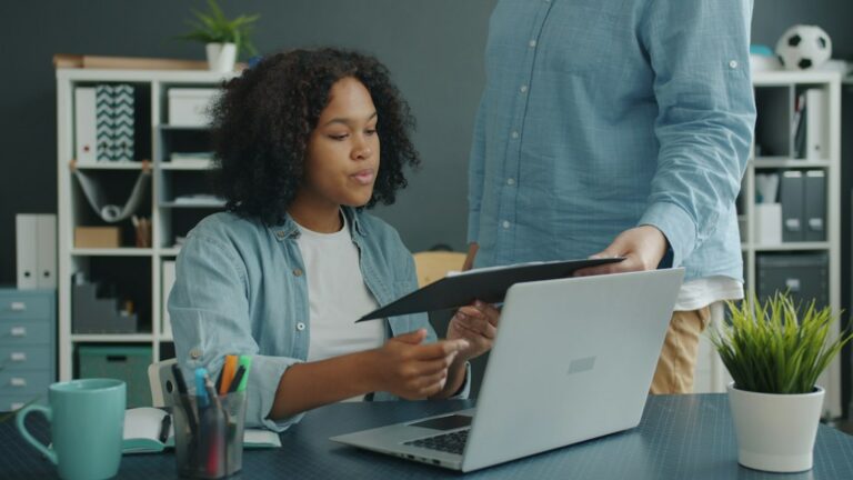 Parent and college student review health insurance documents beside an insurance card and laptop.